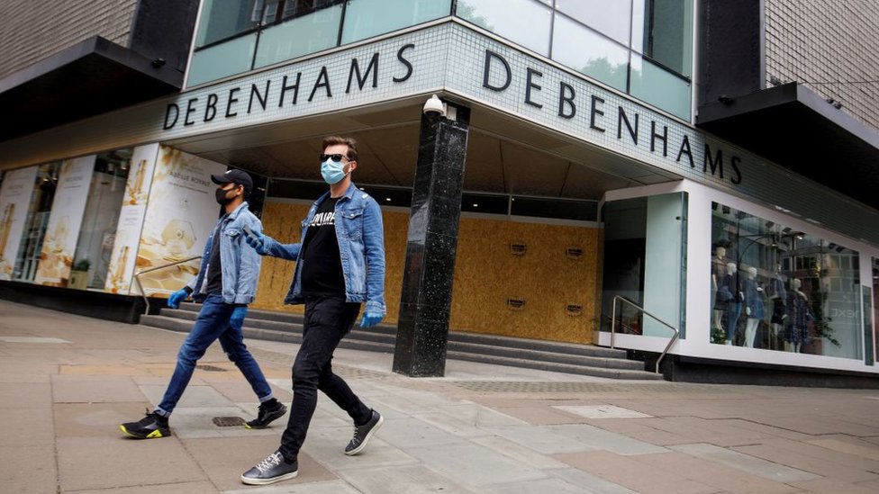 Два человека в масках проходят мимо заколоченного магазина Debenhams на Оксфорд-стрит в Лондоне
