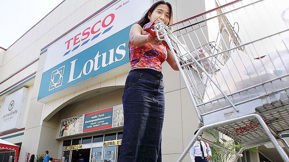 Тайская женщина толкает тележку у входа в тайские магазины британской сети супермаркетов Tesco Lotus в Бангкоке.