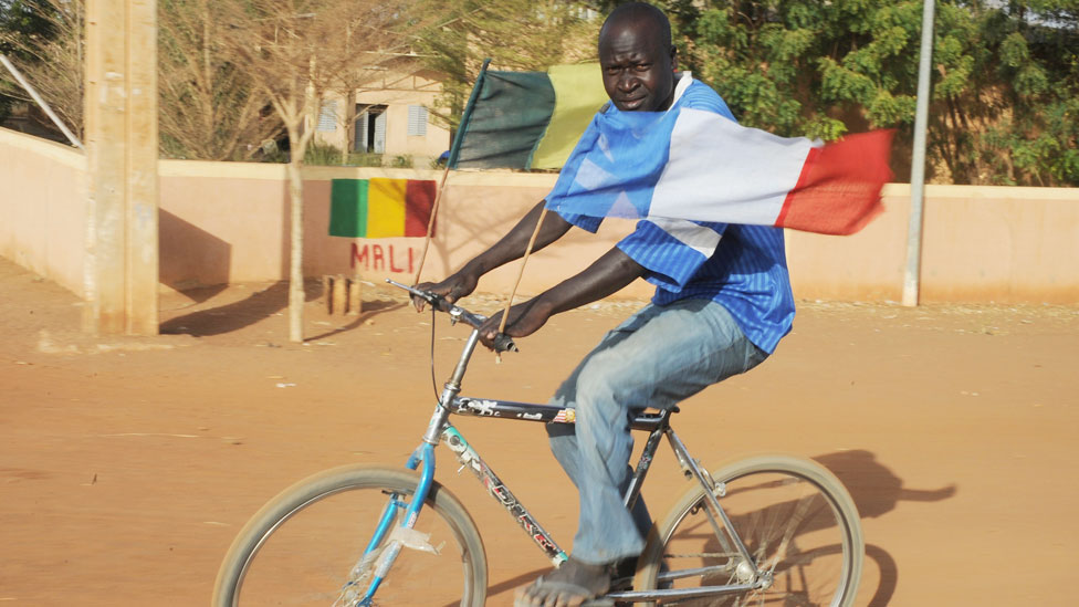 Мужчина из Мали с малийским и французским флагами, развевающимися на велосипеде