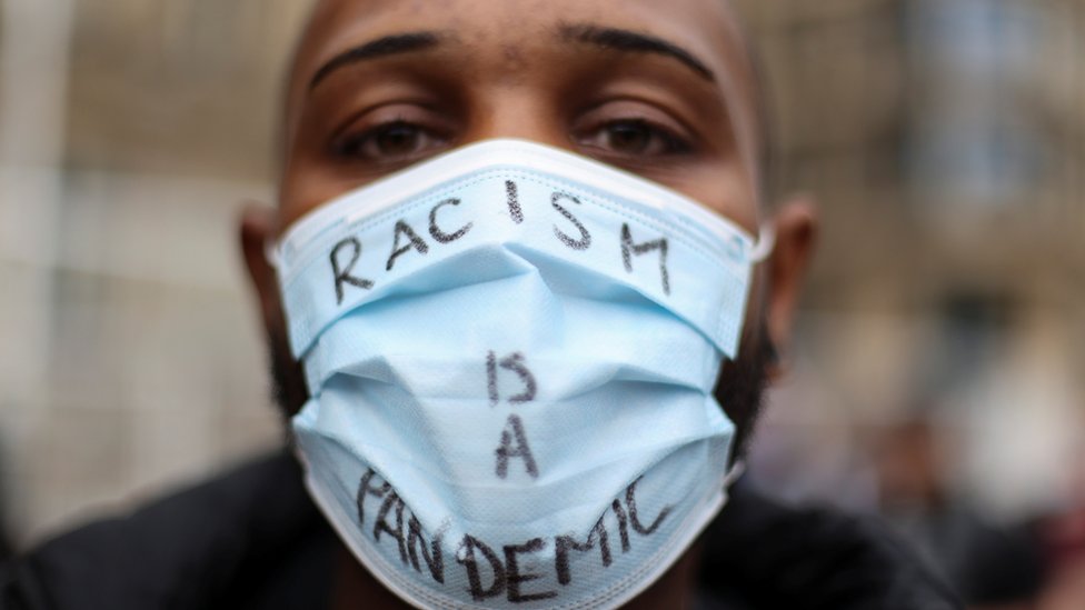 A protester wears a mask saying \