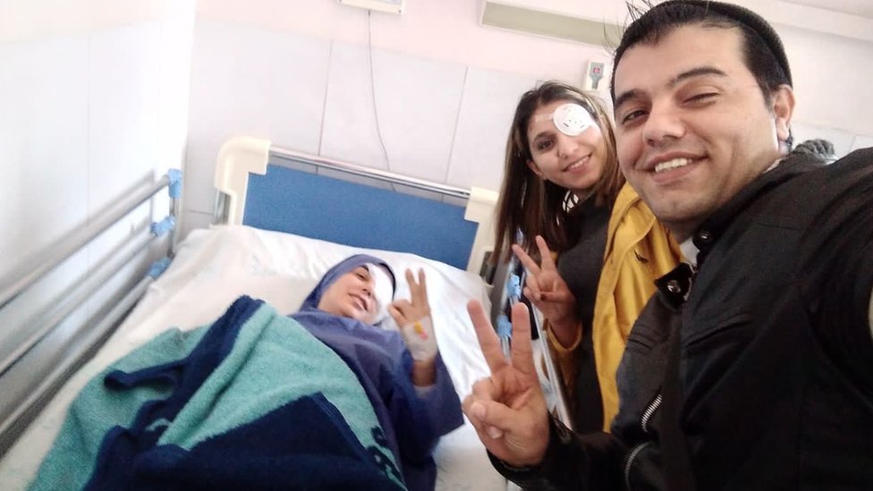 Elahe Tavokolian lying in a hospital bed with Mohammad Farzi and Kosar Eftekhari alongside her