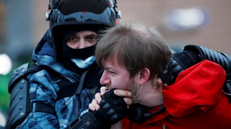A law enforcement officer detains a man while holding him by the face in Moscow