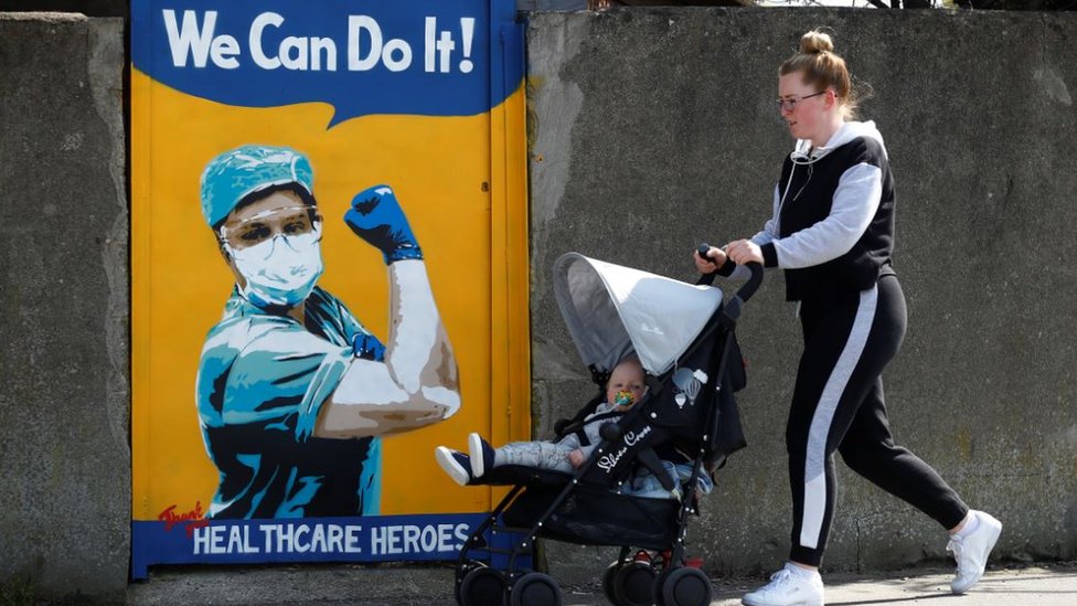 Женщина толкает ребенка в коляске мимо фрески NHS Эммы Блейк в Дублине