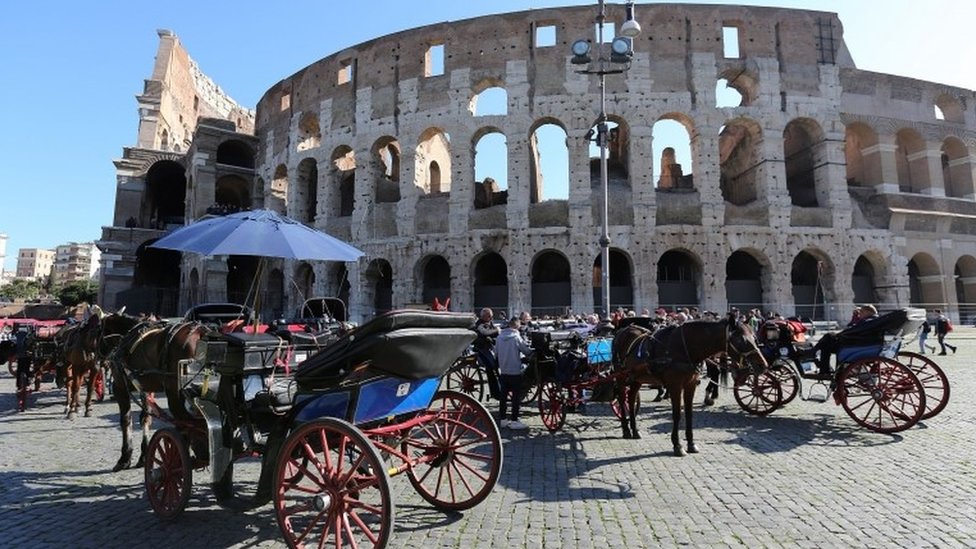 Конные экипажи видны перед древним Колизеем в центре Рима