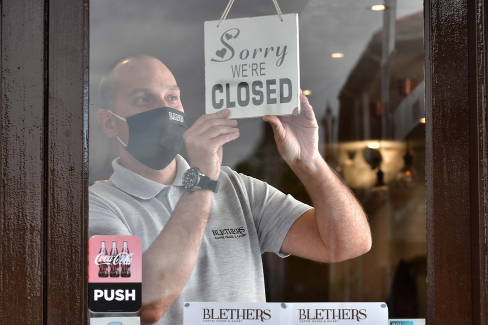 Мужчина ставит табличку «закрыто» в окне своего кафе