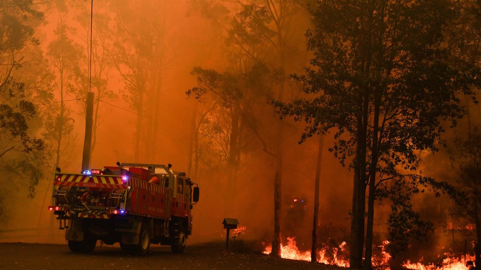 Пожарная машина возле бушующего пожара в Веромби, к юго-западу от Сиднея, на фоне ярко-оранжевого неба