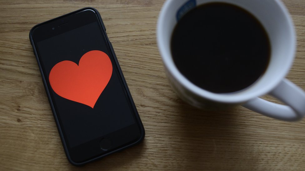 Una taza de café y un teléfono celular con un corazón en la pantalla.