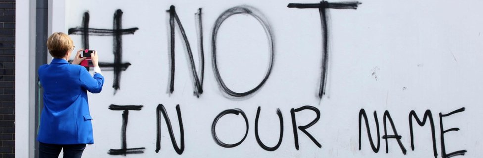 Пешеход делает снимок нового граффити с надписью «# not in our name» в районе Крегган в Дерри (Лондондерри) в Северной Ирландии, недалеко от места, где была смертельно ранена журналистка Лира МакКи