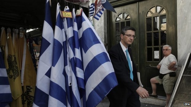 Мужчина проходит мимо прилавка с греческими флагами