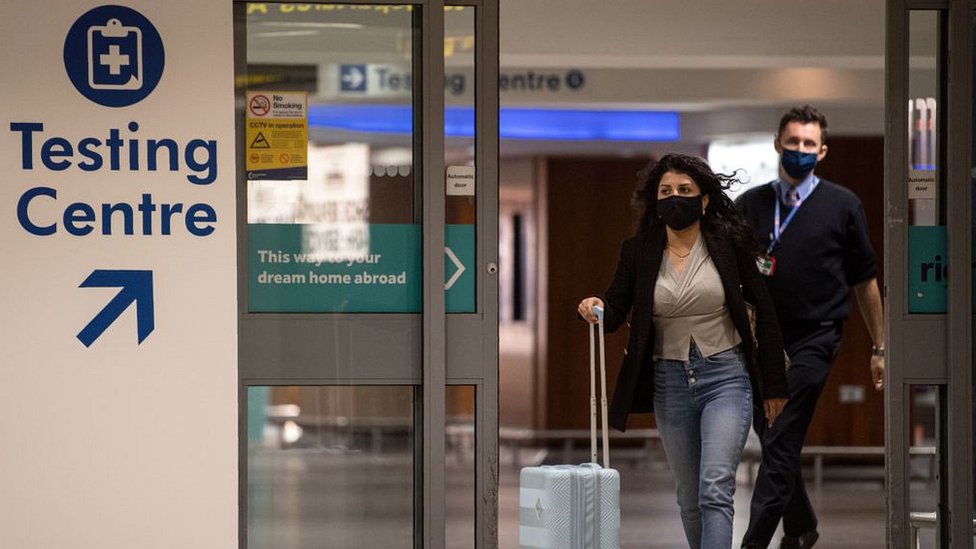 женщина с сумками в аэропорту в маске у знака испытательного центра