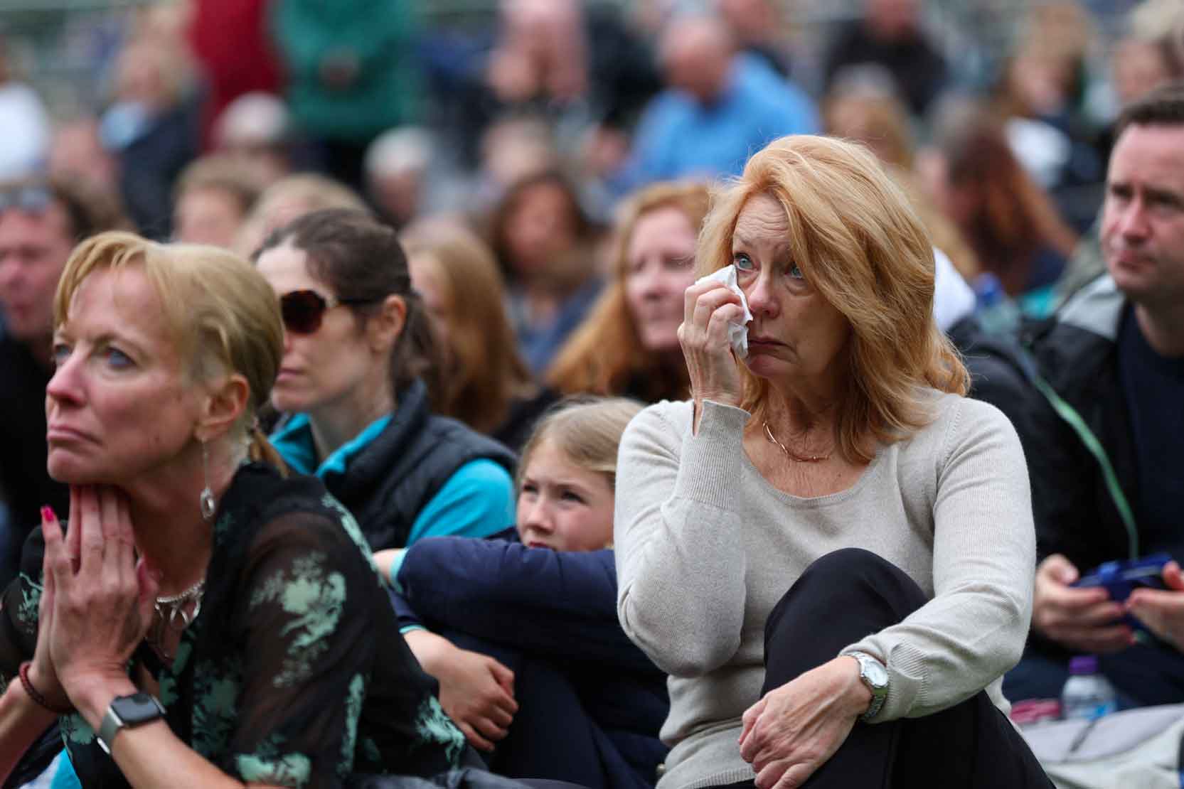 A woman watching the funeral on a big screen wipes away a tear.