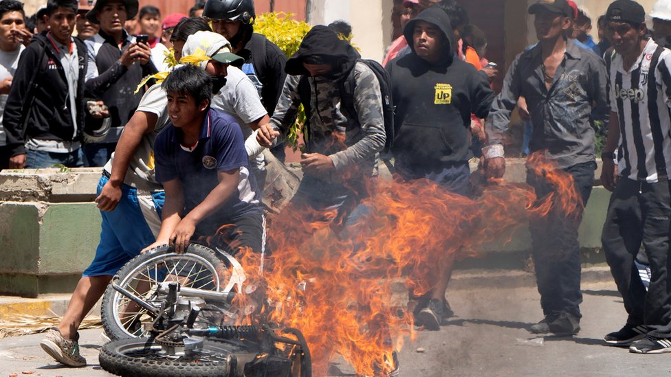 Una motocicleta se quema rodeada por manifestantes.