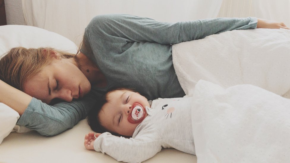 Una mujer duerme en la misma cama con un bebé.