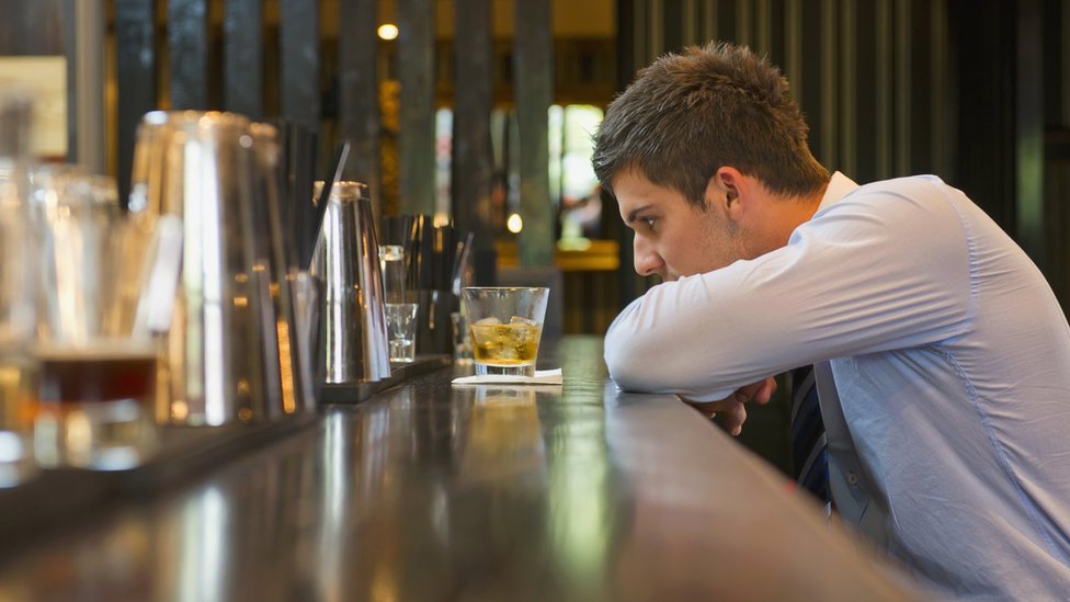 Homem olhando para copo em bar