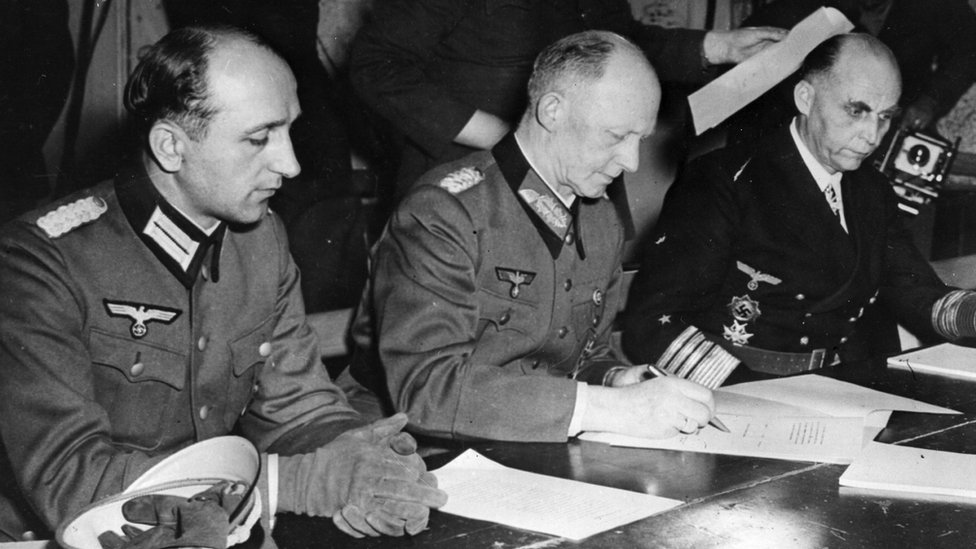 7th May 1945: German soldier and Chief of the Operations Staff Alfred Jodl (1890 - 1946) flanked by his aide on the left and Grand Admiral Hans Georg von Friedeburg on the right, signs the unconditional surrender document imposed by the Allies at General Eisenhower's HQ in Reims.