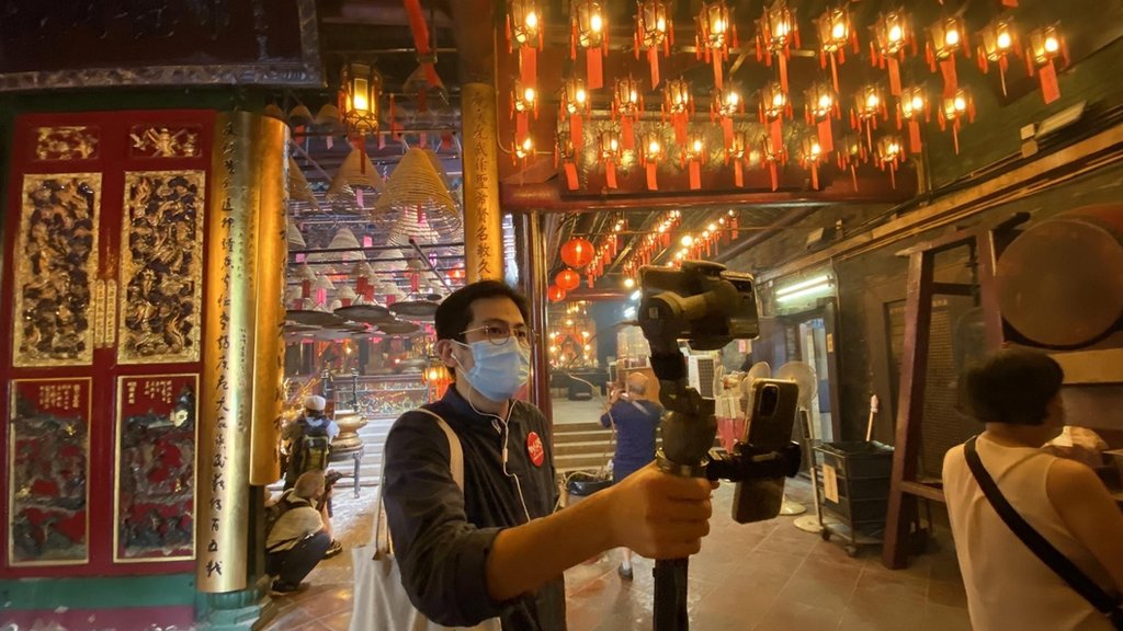 Paul Chan sosteniendo una cámara de transmisión en vivo debajo de linternas eléctricas.