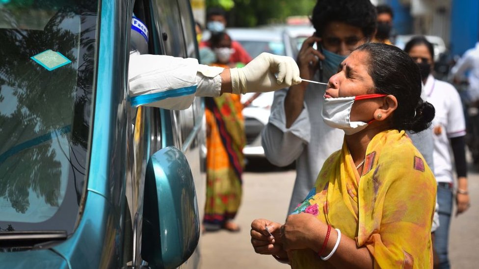 Медицинский работник специальной группы мобильного наблюдения в комбинезоне СИЗ собирает образец мазка у женщины для экспресс-теста на антиген Covid-19 в Модельном Городе 15 июля 2020 года в Нью-Дели, Индия
