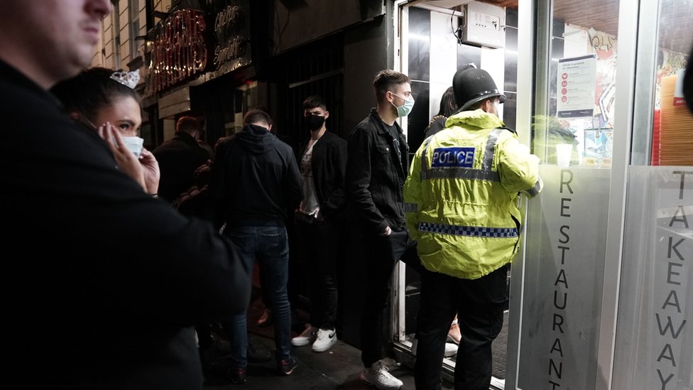 Офицер полиции напоминает рабочим в центре Ньюкасла о комендантском часе в 22:00, который действует в пабах и ресторанах в Англии, чтобы бороться с ростом числа случаев коронавируса.