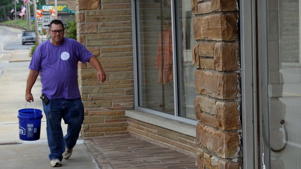 Clint Barta está convencido de que el cambio está al llegar y hará que la alicaída economía local dé un vuelco. Clint Barta con un balde en mano