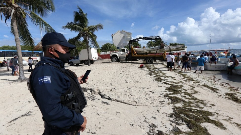Un soldado en la playa de Cancún mientras los pescadores sacan sus botes del agua.