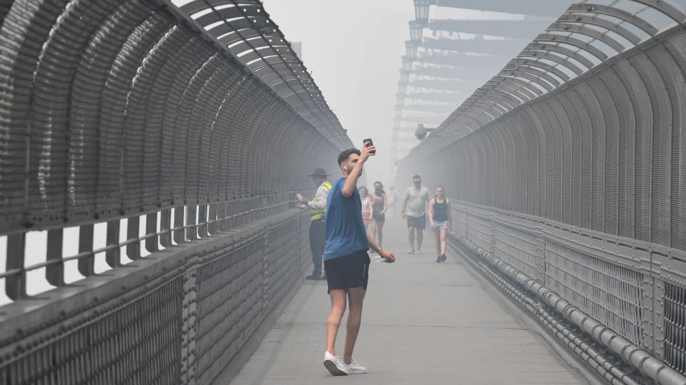 Мужчина делает снимок, когда он пересекает мост Харбор-Бридж в Сиднее среди густого дыма