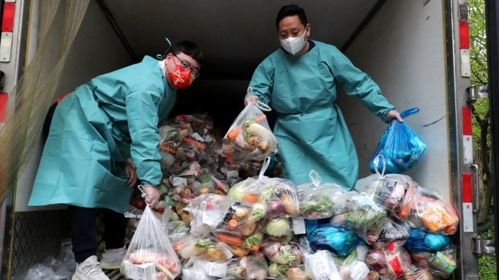 Trabajadores con equipo de protección clasifican bolsas de verduras y comestibles en un camión para distribuirlas a los residentes en un complejo de viviendas durante el cierre en Shanghái el 5 de abril.