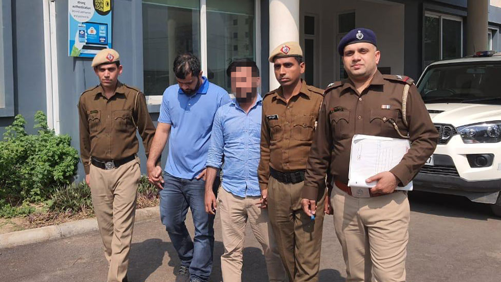 Двое мужчин в синих рубашках окружены индийскими полицейскими у здания