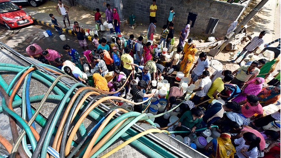 Жители наполняют пустые контейнеры питьевой водой из муниципального танкера в лагере Вивекананд, в Чанакьяпури, 17 апреля в Дели