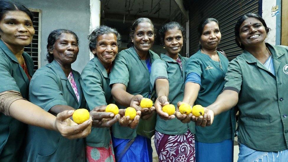Seven of the women sanitation workers holding laddoos in front of them