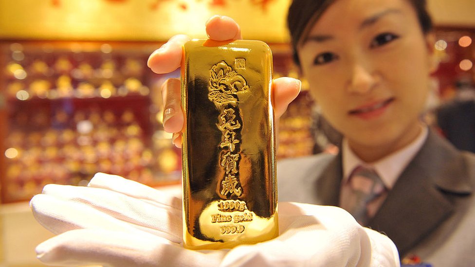 A woman holds a shiny gold bar