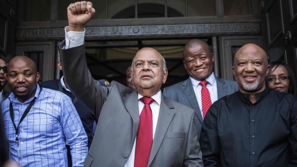 Бывший министр финансов ЮАР Правин Гордхан поднимает кулак, обращаясь к группа сторонников за пределами Национального казначейства Южной Африки в Претории