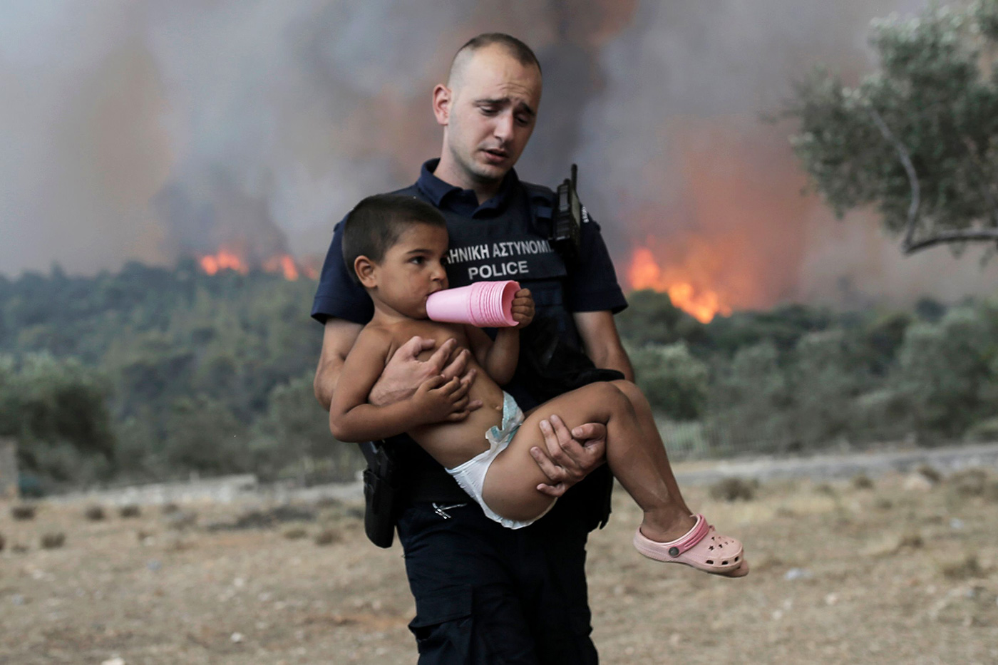 ​​A police officer carries a child away from a wildfire in the Attica region of Greece - 18 July 2023