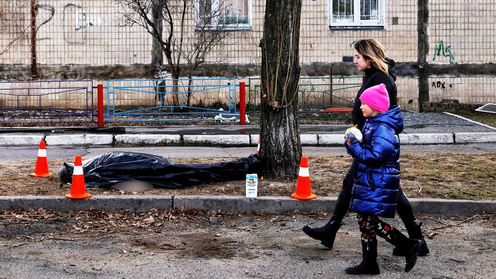 A woman and a child walk past a dead body in front of a residential building that was hit by a shell in Kyiv, 14 March 2022