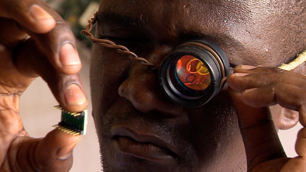 Gnikou Afate, pendiri laboratorium Woora Make, memeriksa sebuah microchip menggunakan kaca pembesar ala kadarnya