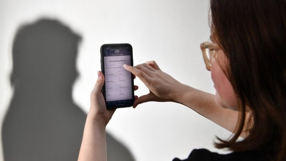 Постановочная фотография человека, использующего приложение правительства Австралии для отслеживания коронавируса на телефоне