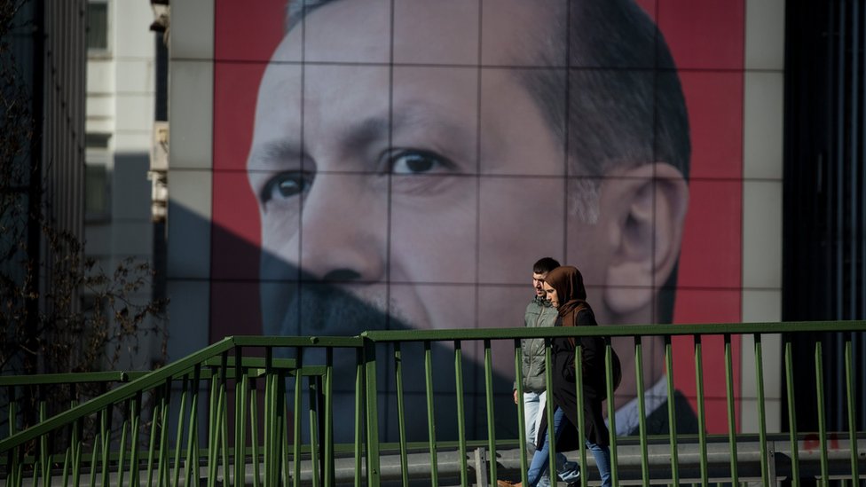 Una victoria fortalecería muchísimo a Erdogan, Pero una derrota no implicaría su final. Una pareja camina frente a un gigantesco letrero con la imagen de Erdogan.