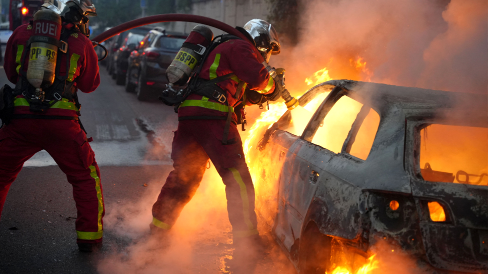 Firefighter extinguish a burning vehicle destroyed by protesters in Nanterre, west of Paris, on 27 June 2023