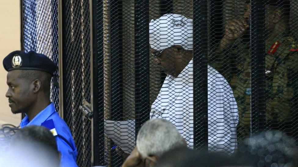 Свергнутый военный правитель Судана Омар аль-Башир стоит в клетке подсудимого во время открытия судебного процесса по делу о коррупции в Хартуме 19 августа 2019 г.