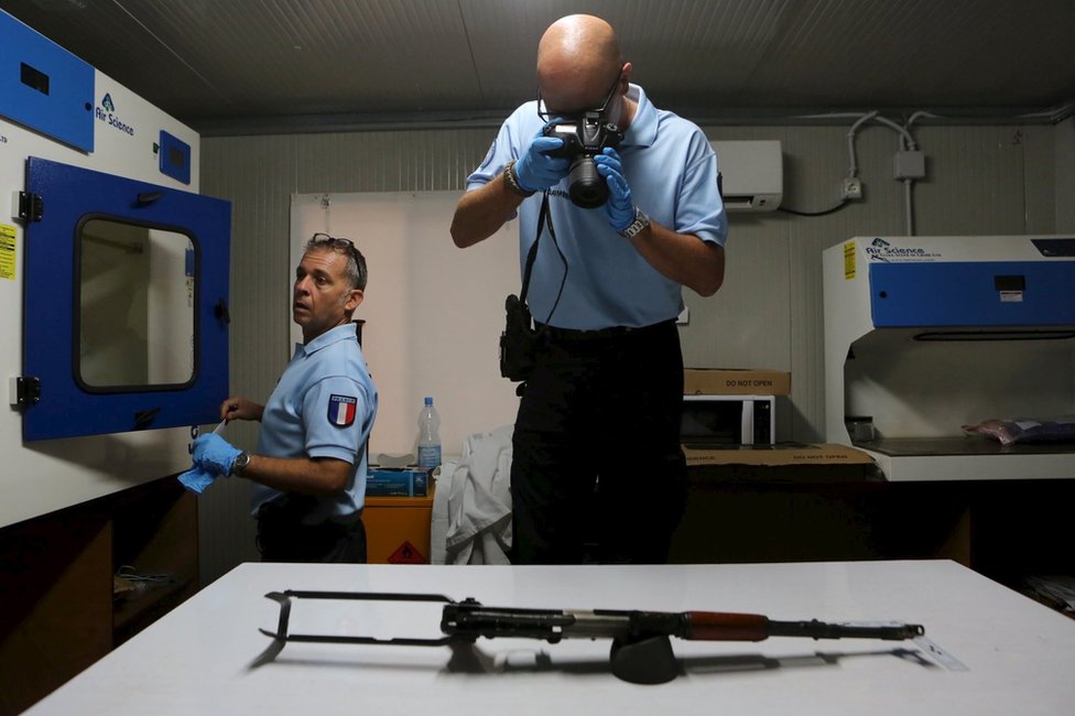 Французский жандарм, работающий на ООН, фотографирует АК-47, использованный боевиками при нападении на отель Radisson Blu, на столе в лаборатории в Бамако, Мали