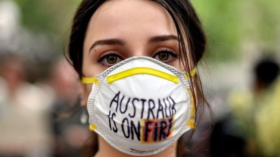 Женщина в маске говорит, что Австралия горит во время протеста против изменения климата