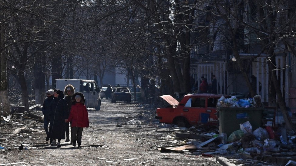 Los residentes locales caminan cerca de los edificios residenciales que resultaron dañados durante el conflicto entre Ucrania y Rusia en la sitiada ciudad portuaria de Mariupol.