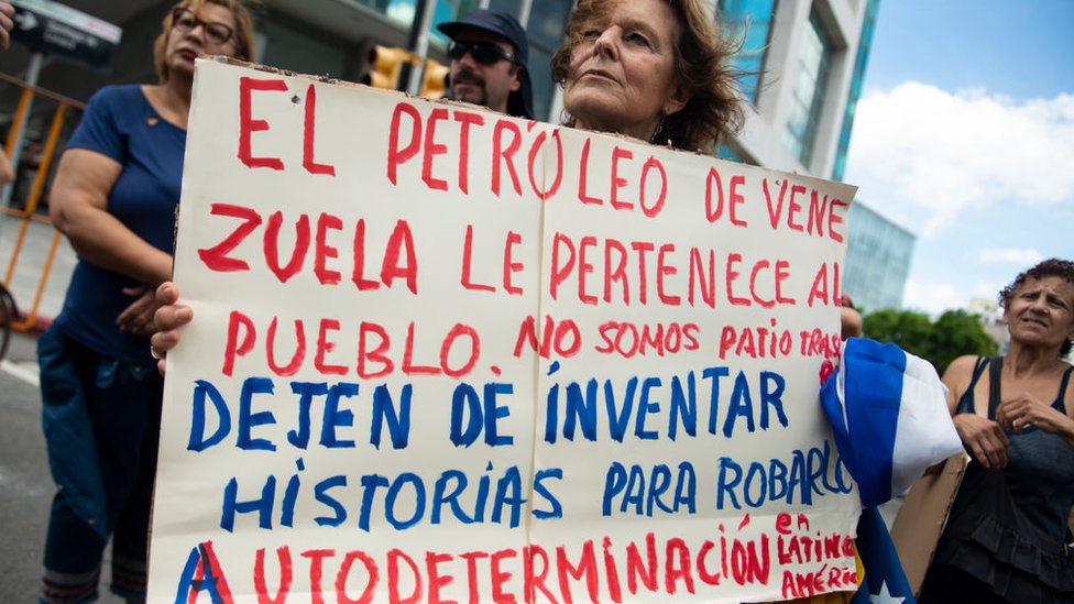Mujer protestando con letrero que dice: "El petróleo de Venezuela le pertenece al pueblo"