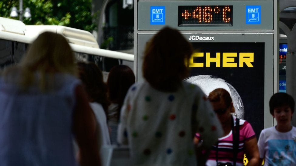 Люди проходят мимо городской цифровой доски, показывающей 46 градусов Цельсия на автобусной остановке в Мадриде