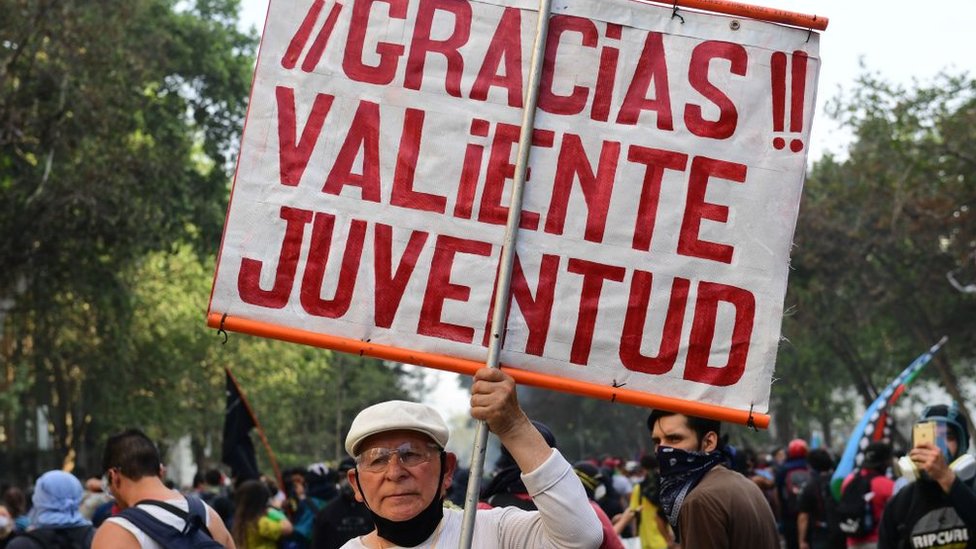 Hombre de edad sostiene letrero en protestas en chile