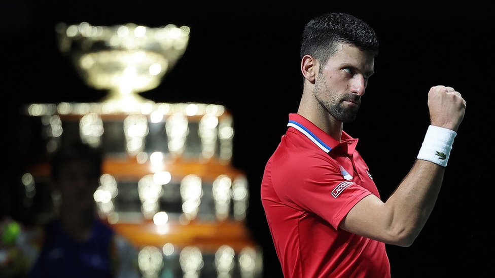 Novak Djokovic pumps his fist with the Davis Cup trophy visible in the background