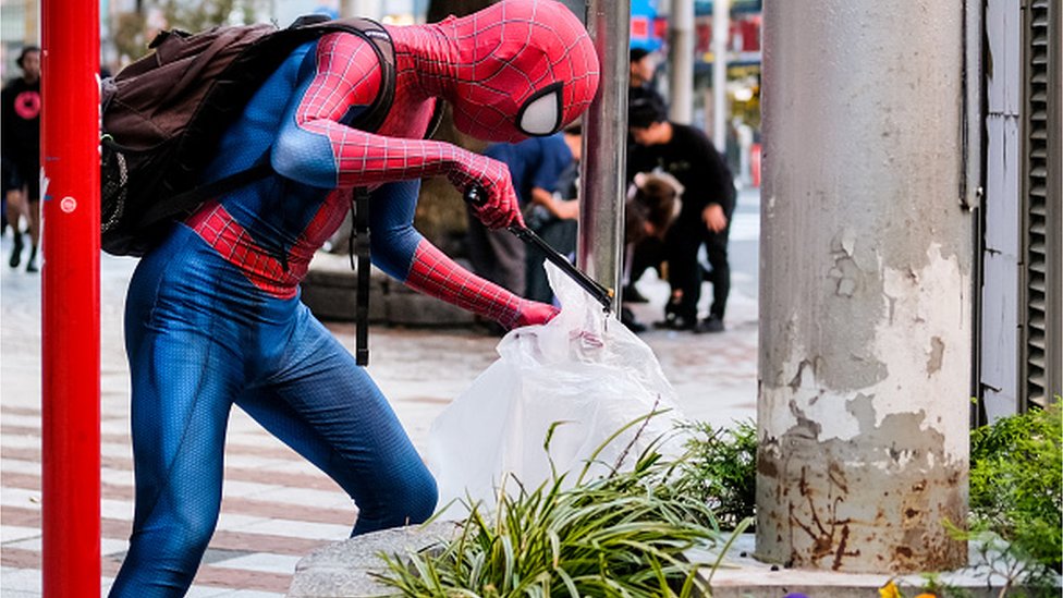 Person dressed as Spider-Man helps clean the streets the day after Halloween celebrations