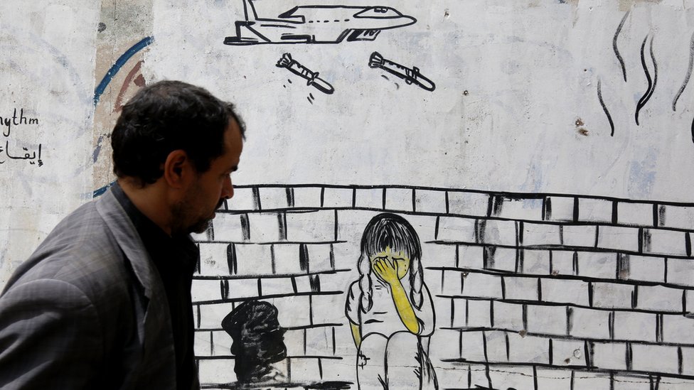 Мужчина проходит мимо стены, покрытой граффити с изображением военного самолета, сбрасывающего бомбы на ребенка, в Сане, Йемен (10 августа 2018 г.)