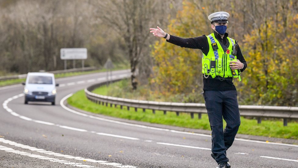 Изоляция: Офицер полиции Дайфед-Поуис указывает на машину, чтобы остановиться во время проверок во время важных поездок в Кармартеншире