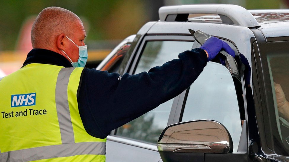 Сотрудник NHS передает тестовый набор человеку в машине