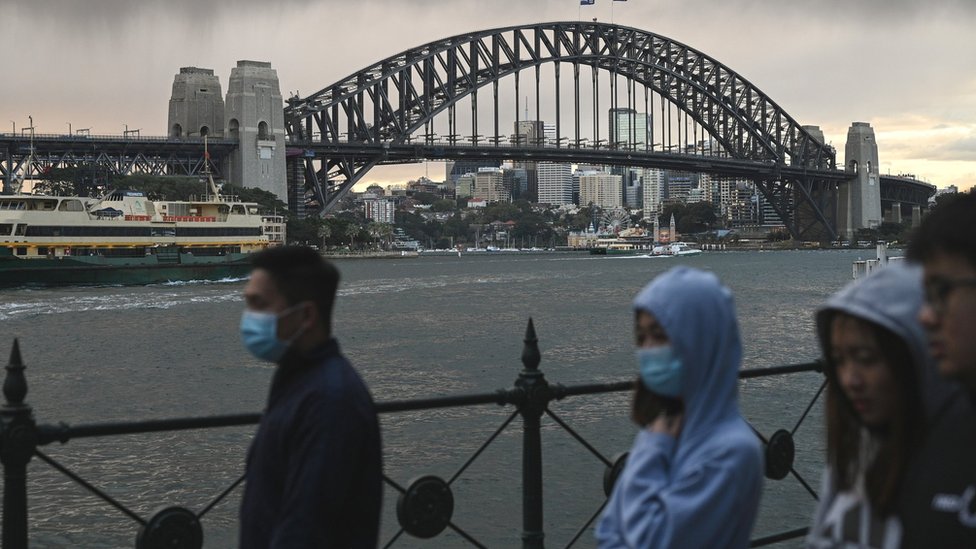 Люди в масках идут перед мостом через гавань Сиднея
